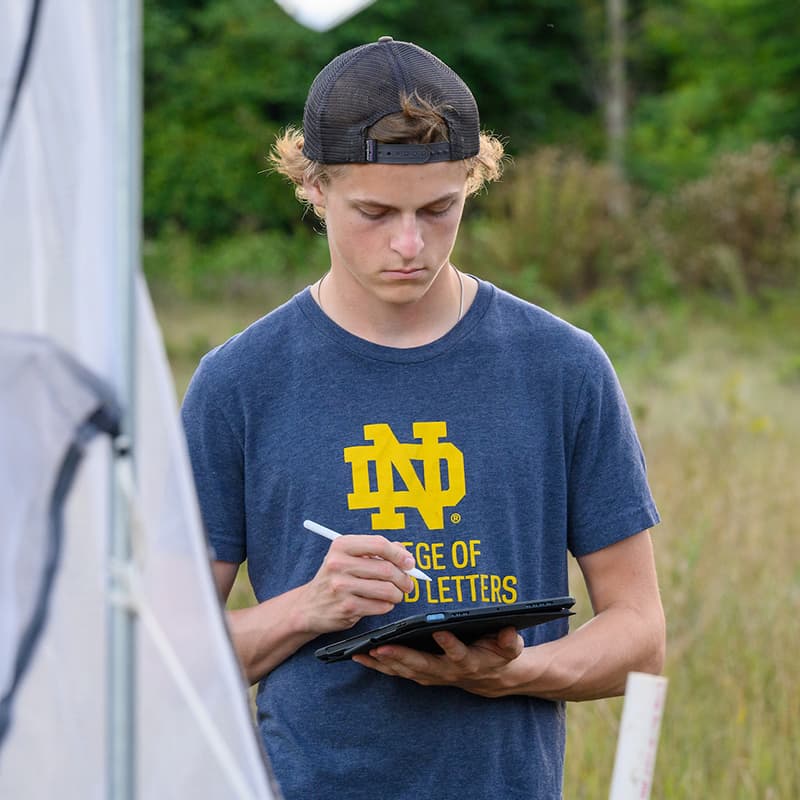 Notre Dame student takes notes while standing in field
