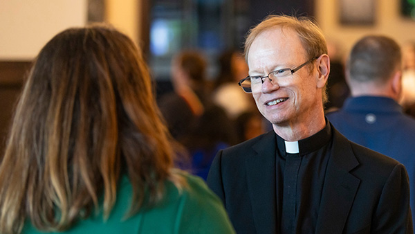 Rev. Robert A. Dowd, C.S.C. smiling while speaking with a woman