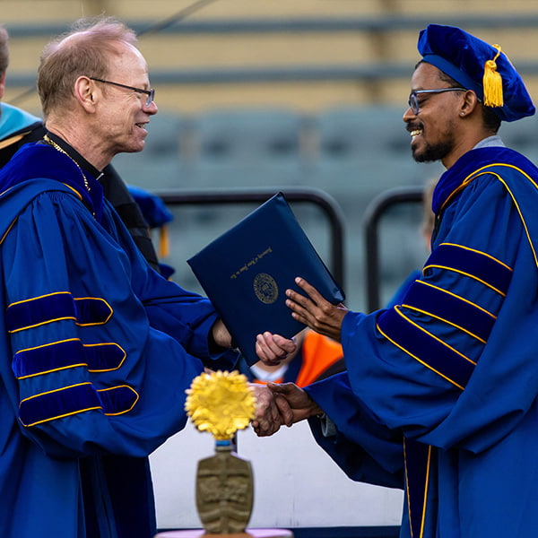 Rev. Robert A. Dowd, C.S.C. handing a diploma to a man during Notre fDame’s commencement ceremony.