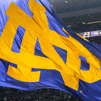 A navy blue Notre Dame flag with a gold monogram flying in the Stadium