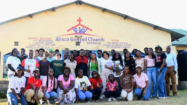 Large group of people smiling in front of a yellow building with Africa Gospel Church on the side