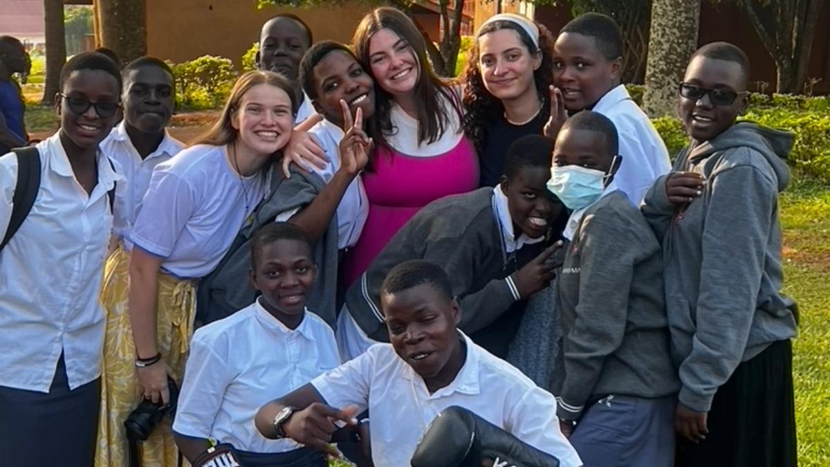 Group of Ugandan students standing with Notre Dame students in a group outside, many holding up two fingers in a peace sign
