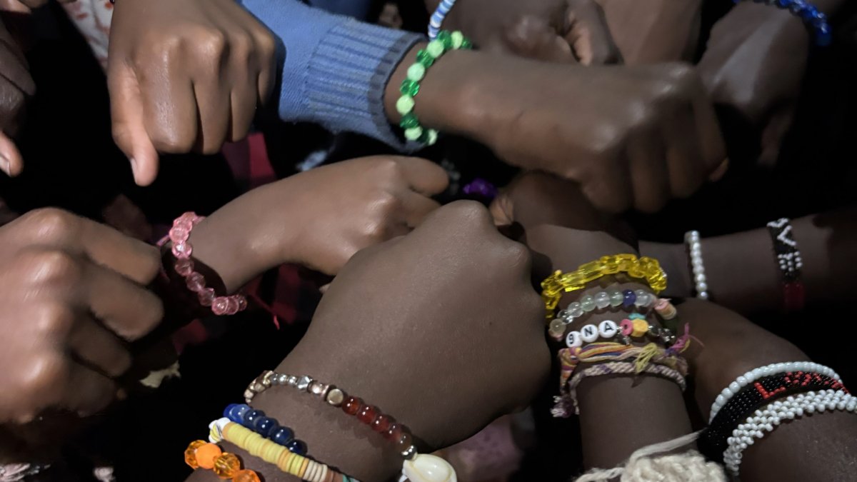 Group of hands together in a circle, all wearing bracelets of different colors