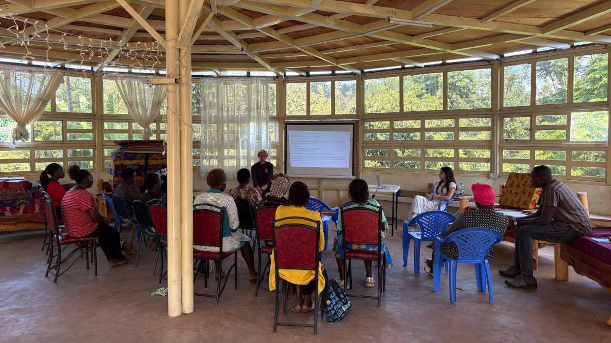 Group of people sitting in a wooden structure, facing one person and a projected screen of text