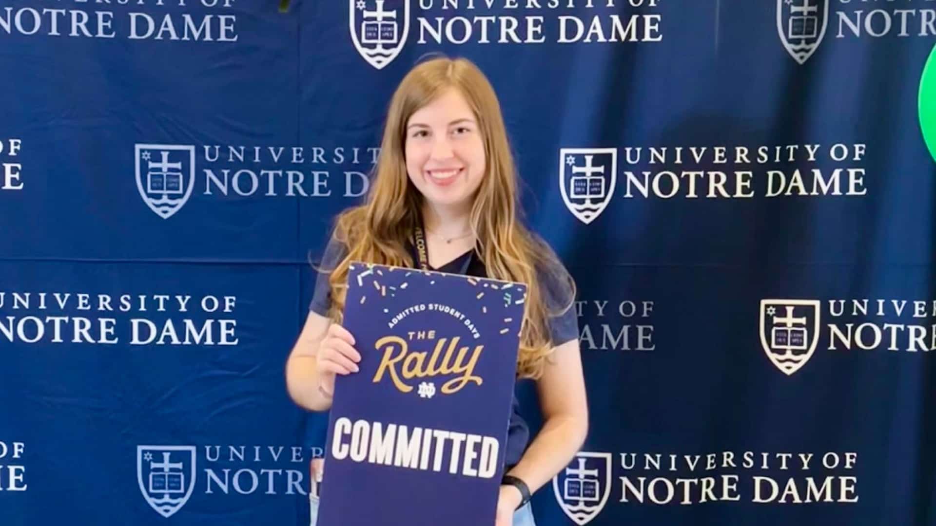 Ryan Fitchpatrick smiles while holding a sign celebrating her commitment to attend Notre Dame.