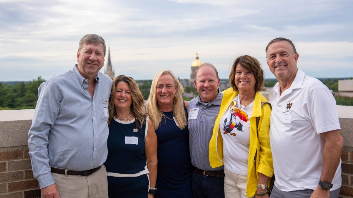 Group of six adults smiling while standing outside on a tall building with a Golden Dome in the background